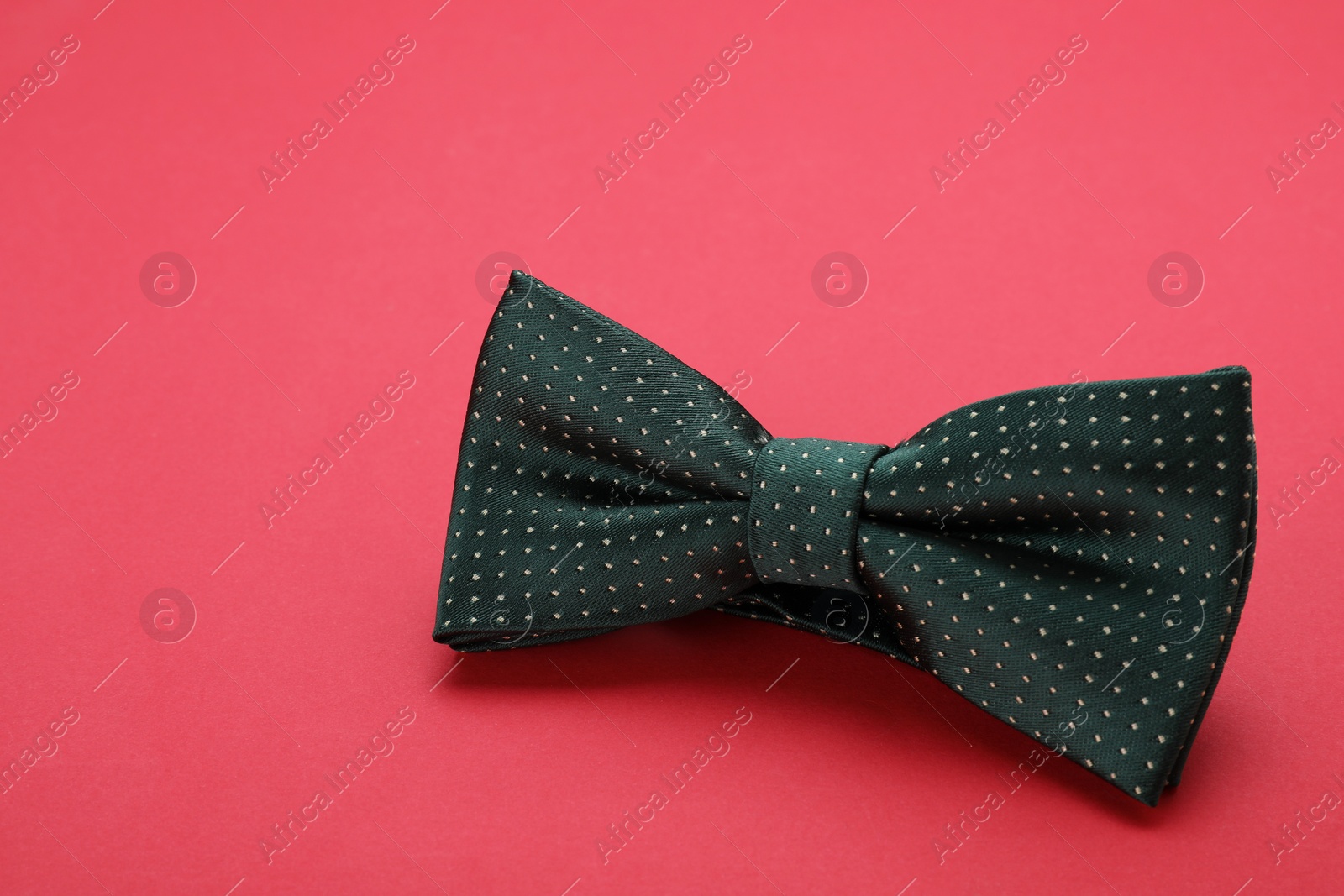 Photo of Stylish black bow tie with polka dot pattern on red background, space for text