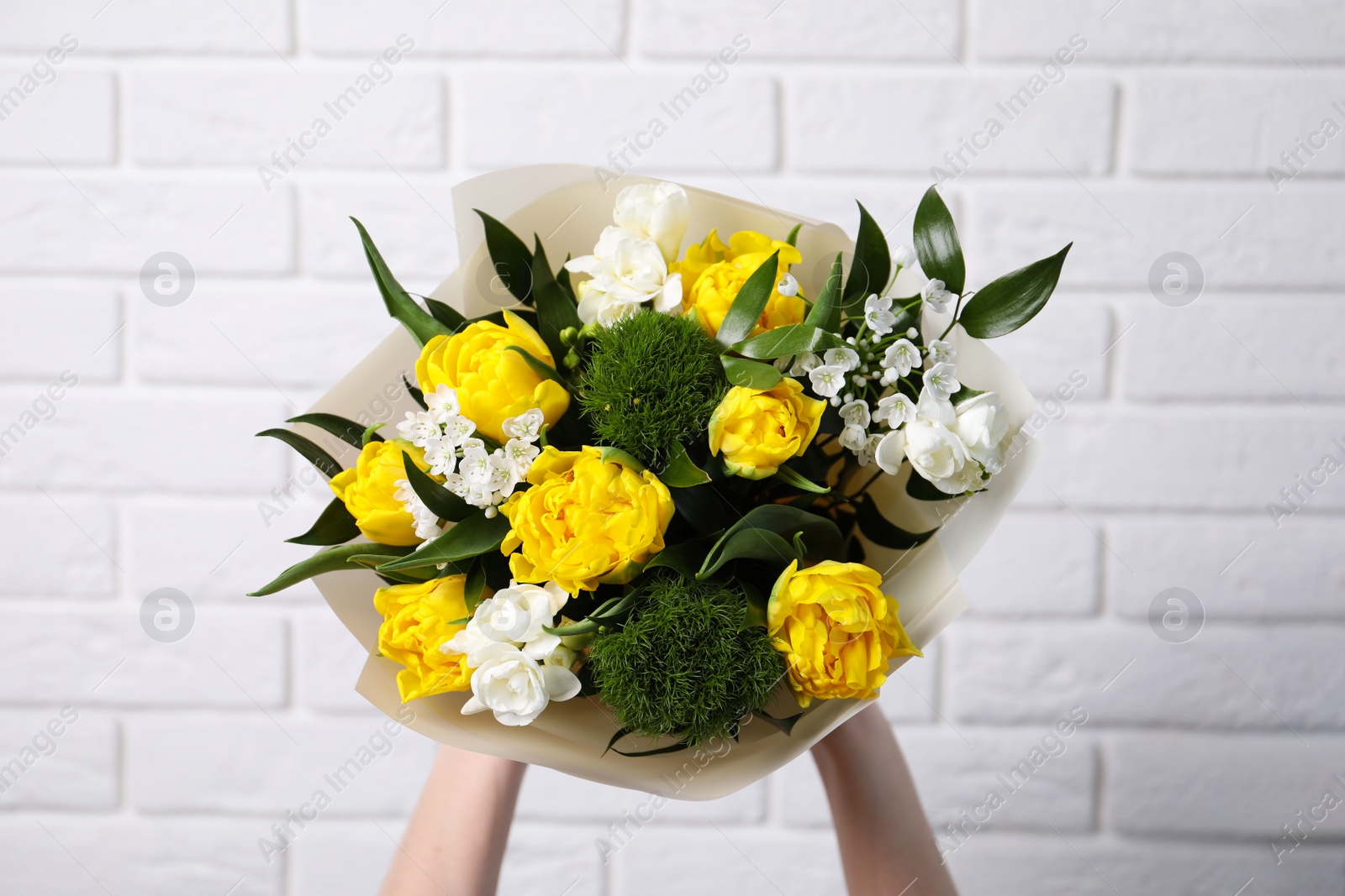 Photo of Woman with bouquet of beautiful tulips near white brick wall, closeup