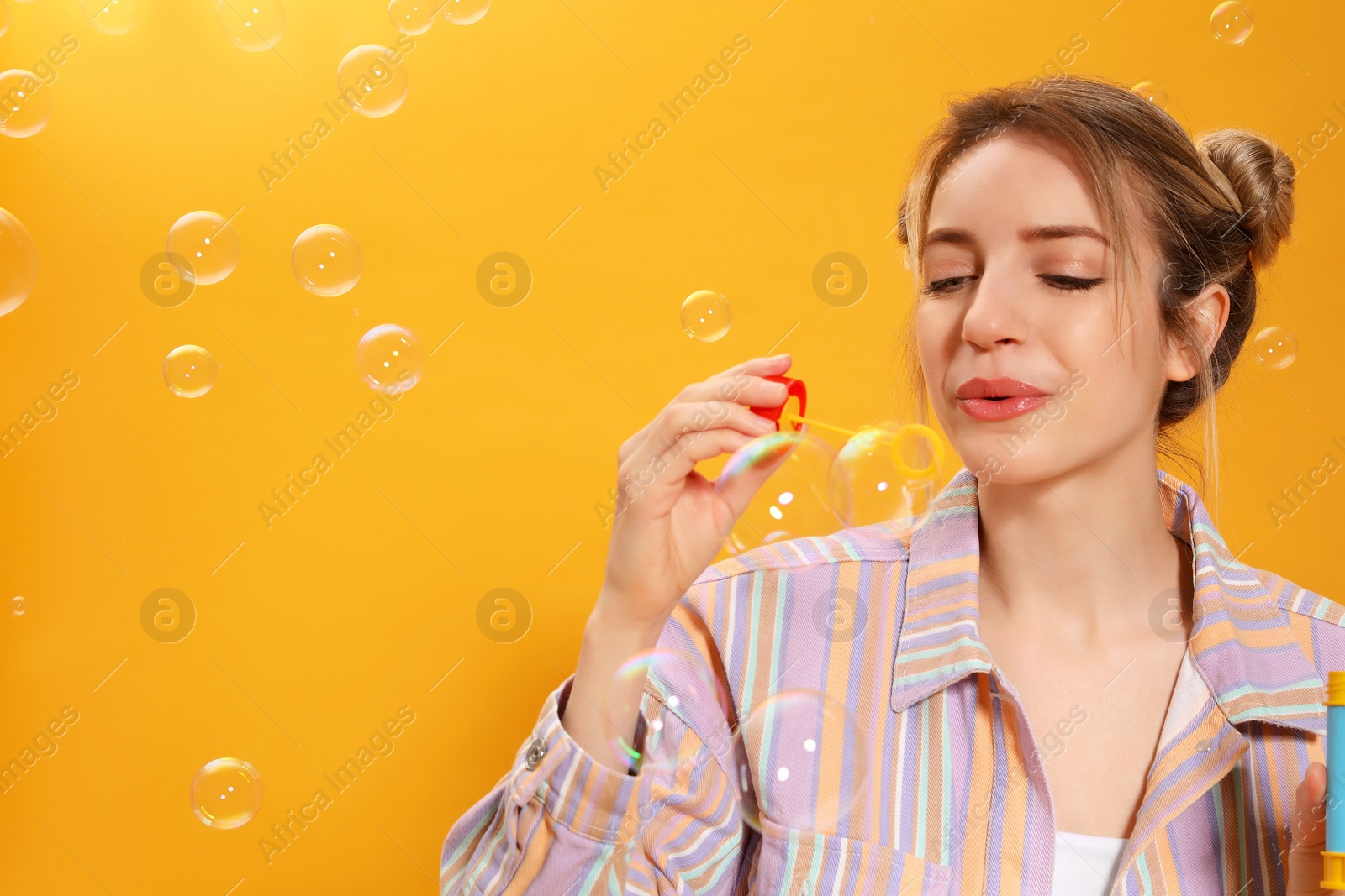 Photo of Young woman blowing soap bubbles on yellow background, space for text