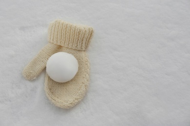 Knitted mitten and snowball on snow outdoors, top view. Space for text