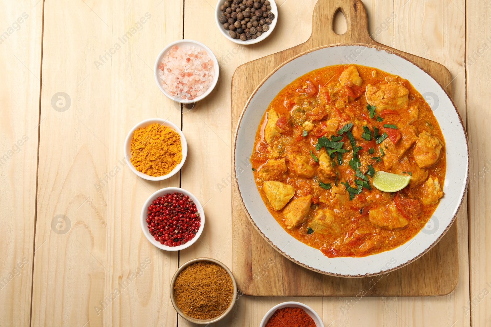 Photo of Delicious chicken curry and spices on wooden table, flat lay. Space for text