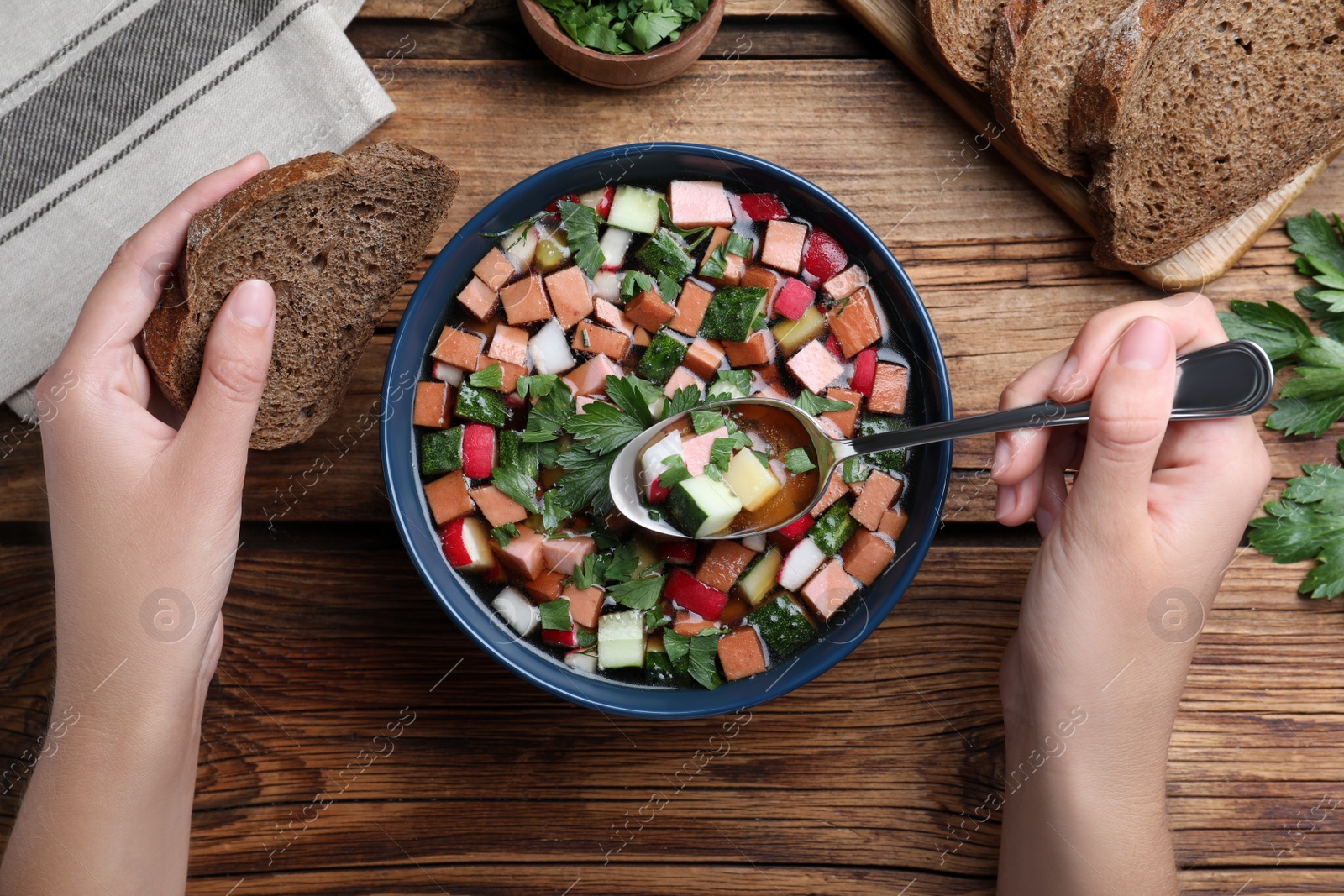 Photo of Woman eating delicious cold okroshka with kvass at wooden table, top view. Traditional Russian summer soup