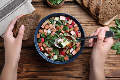 Woman eating delicious cold okroshka with kvass at wooden table, top view. Traditional Russian summer soup