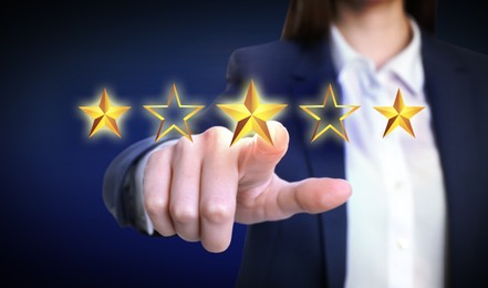 Quality evaluation. Businesswoman touching virtual golden star on blue background, closeup