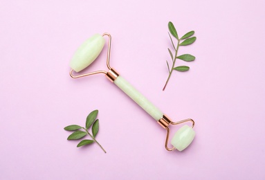 Natural face roller and leaves on pink background, flat lay