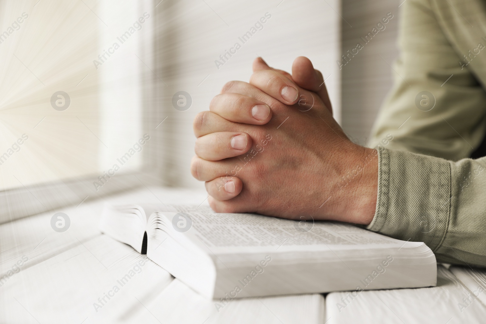 Image of Religion. Christian man praying over Bible at table, closeup