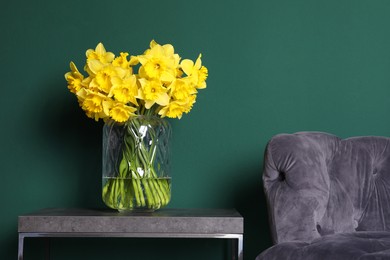 Beautiful daffodils in vase on table near green wall indoors