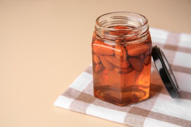 Photo of Jar with almonds and honey on beige table, space for text