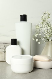 Photo of Bath accessories. Personal care products and gypsophila flowers in vase on gray table near white marble wall