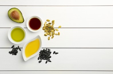 Vegetable fats. Different cooking oils in bowls and ingredients on white wooden table, flat lay. Space for text