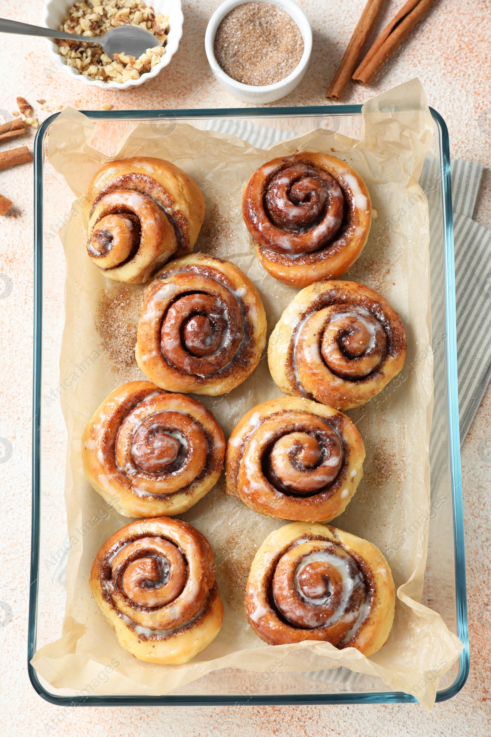 Photo of Tasty cinnamon rolls, sticks and nuts on beige textured table, flat lay