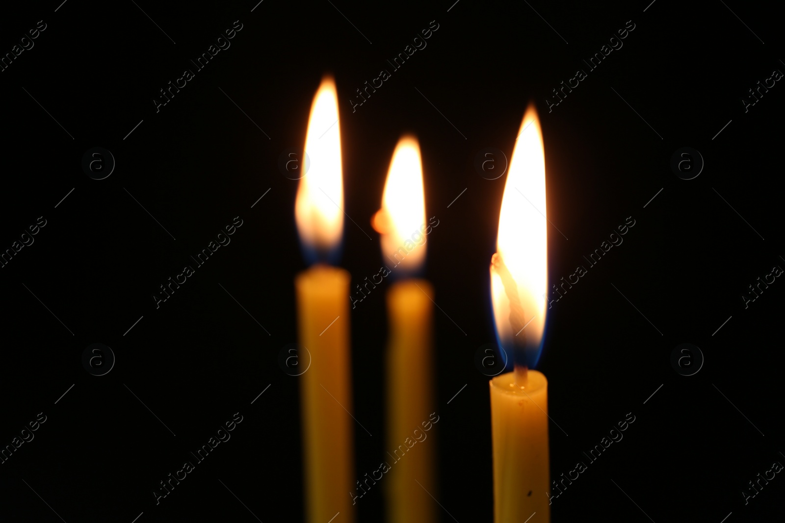 Photo of Burning church candles on dark background, closeup. Space for text