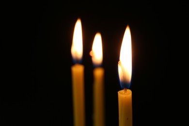 Photo of Burning church candles on dark background, closeup. Space for text