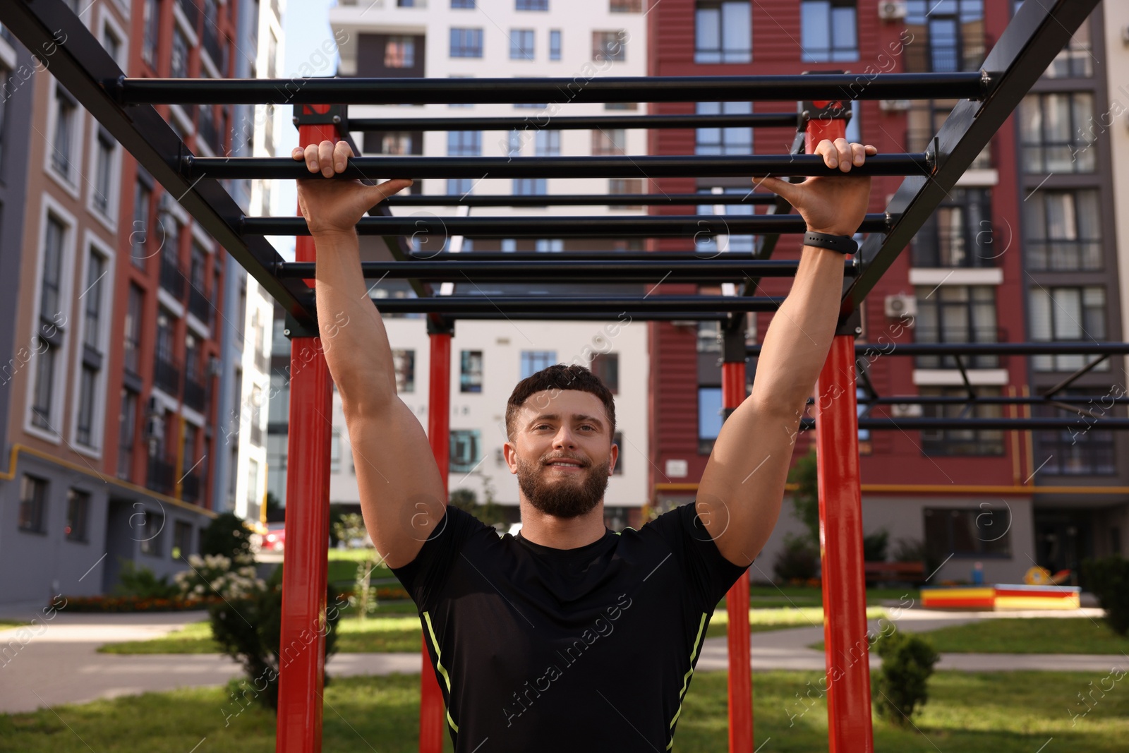 Photo of Smiling man training on monkey bars at outdoor gym