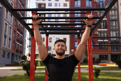 Smiling man training on monkey bars at outdoor gym