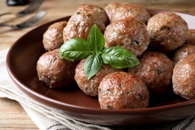 Photo of Tasty cooked meatballs with basil served on wooden table, closeup