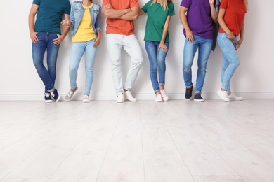 Photo of Group of young people in jeans and colorful t-shirts near light wall