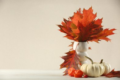 Photo of Beautiful autumn leaves in vase, pumpkins and physalis on table against beige background, space for text