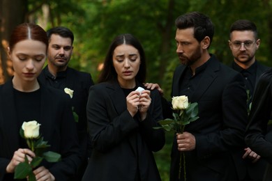 Photo of Funeral ceremony. Sad people with white rose flowers mourning outdoors