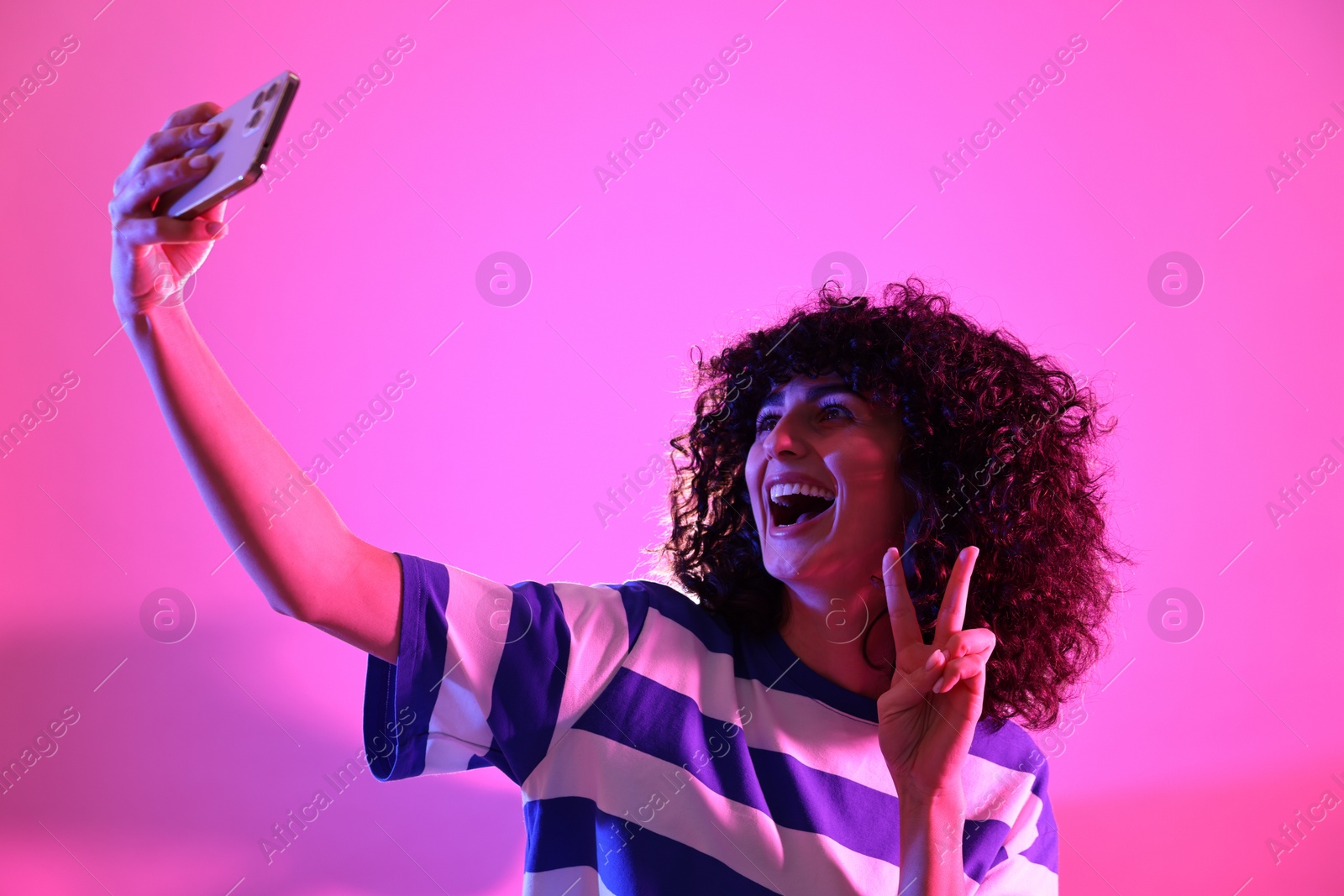 Photo of Beautiful young woman taking selfie on color background in neon lights