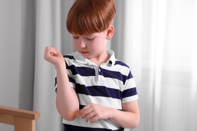 Photo of Little boy putting sticking plaster onto elbow indoors