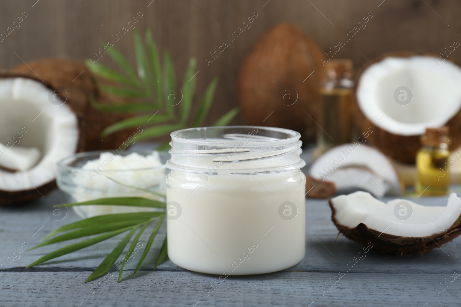 Photo of Jar of organic coconut cooking oil, leaves and fresh fruits on grey wooden table, closeup