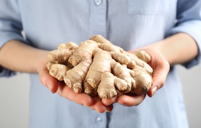 Woman holding pile of ginger roots on light background, closeup. Natural antibiotic