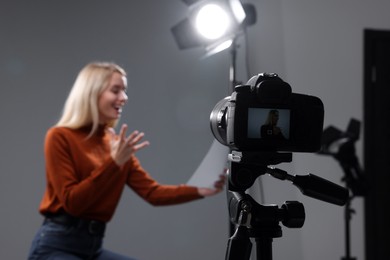 Photo of Casting call. Emotional woman with script sitting on chair and performing in front of camera against grey background in studio, selective focus