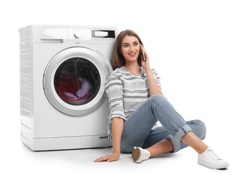 Young woman talking on phone while doing laundry against white background