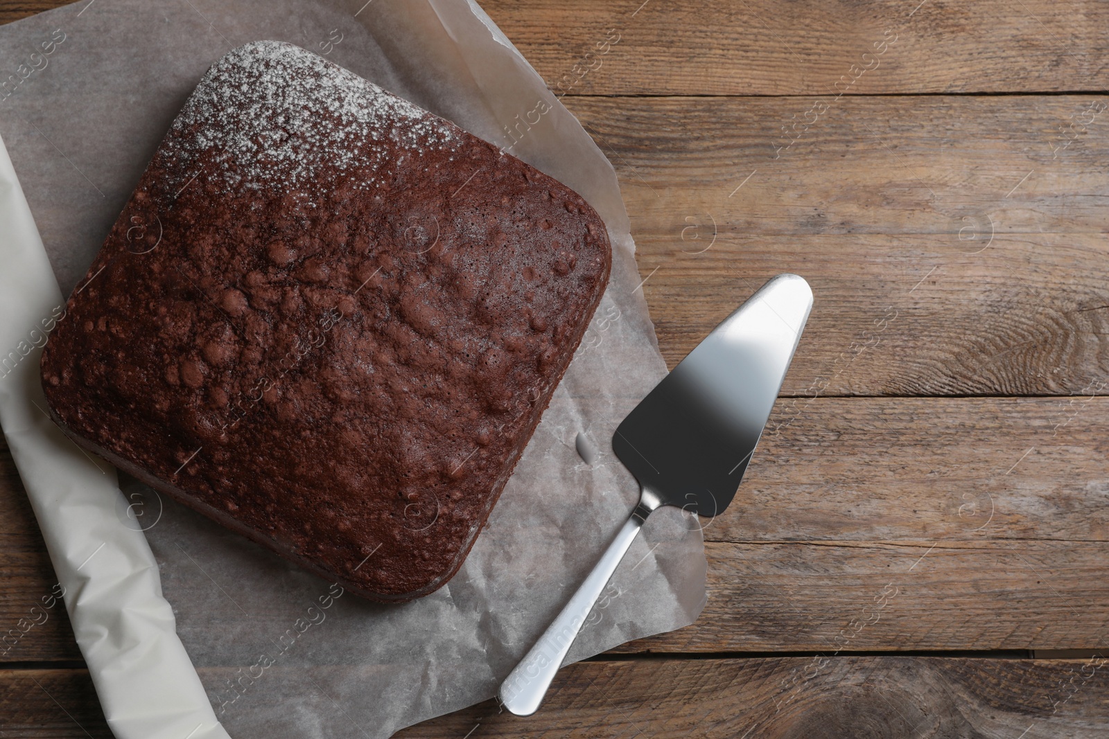 Photo of Homemade chocolate sponge cake and spatula on wooden table, flat lay. Space for text