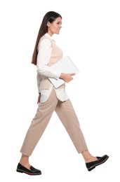 Young woman with laptop walking on white background