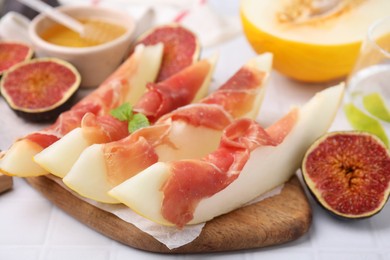 Photo of Tasty melon, jamon and figs served on white tiled table