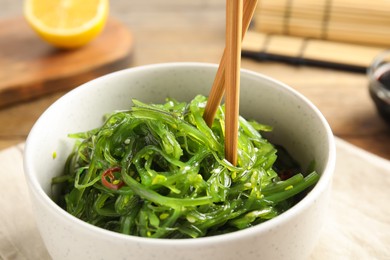Photo of Japanese seaweed salad with chopsticks served on table, closeup