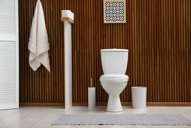 White toilet bowl near wooden wall in modern bathroom interior