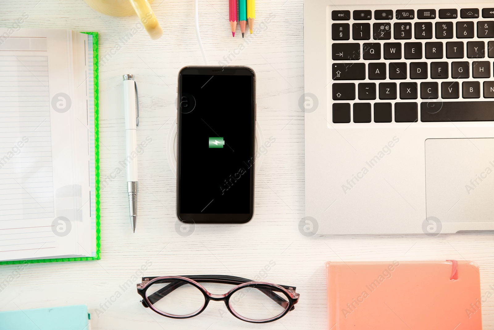 Photo of Flat lay composition with mobile phone and wireless charger on white wooden table. Modern workplace accessory