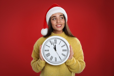 Photo of Woman in Santa hat with clock on red background. New Year countdown