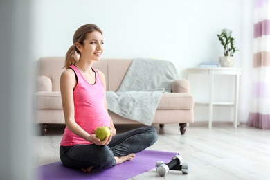 Photo of Young pregnant woman with apple at home