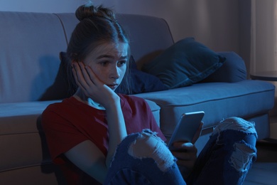 Photo of Shocked teenage girl with smartphone in dark room. Danger of internet