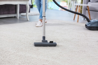 Photo of Woman removing dirt from carpet with vacuum cleaner indoors, closeup