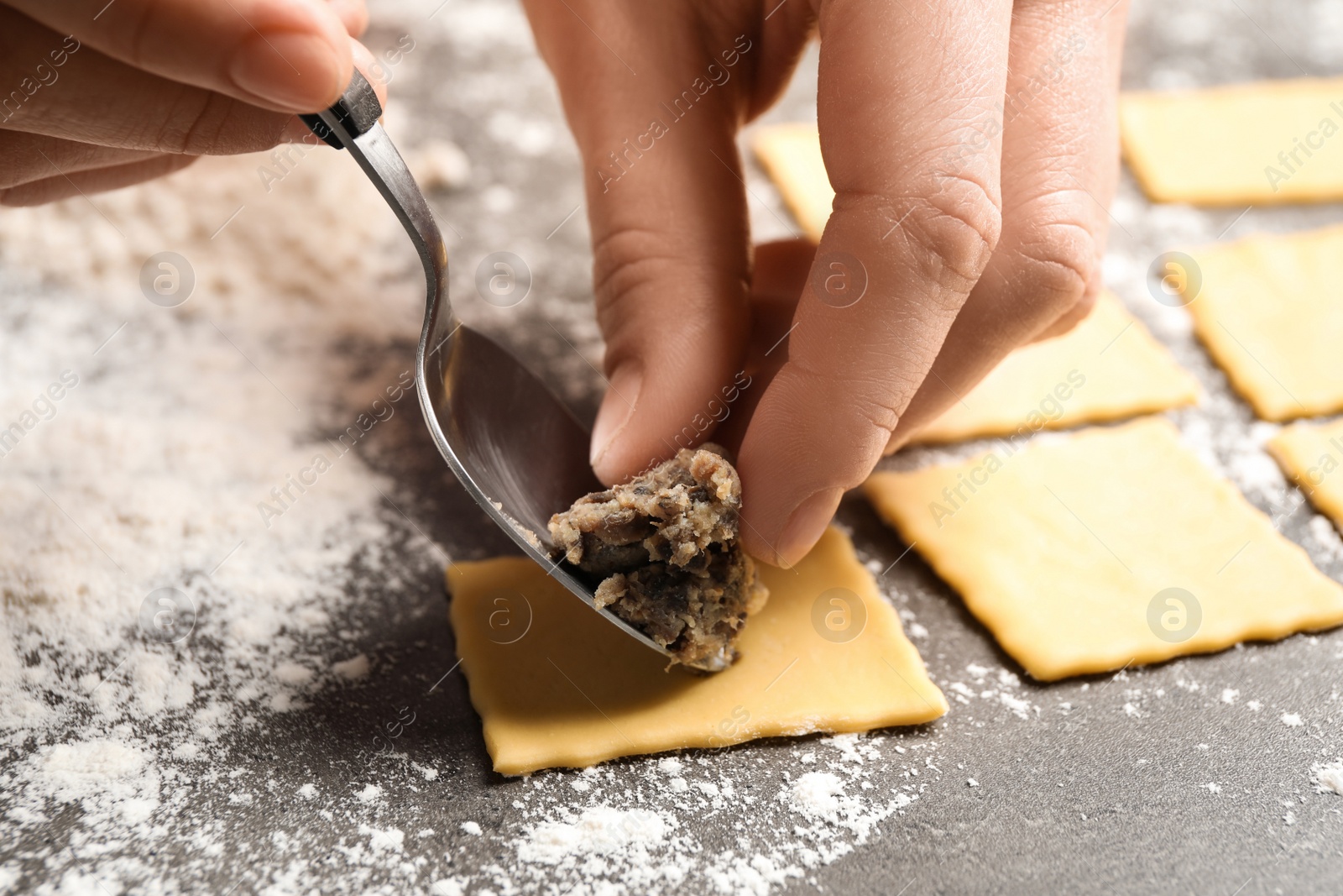 Photo of Woman making ravioli at grey table, closeup. Italian pasta