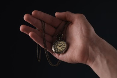 Photo of Man holding chain with elegant pocket watch on black background, closeup