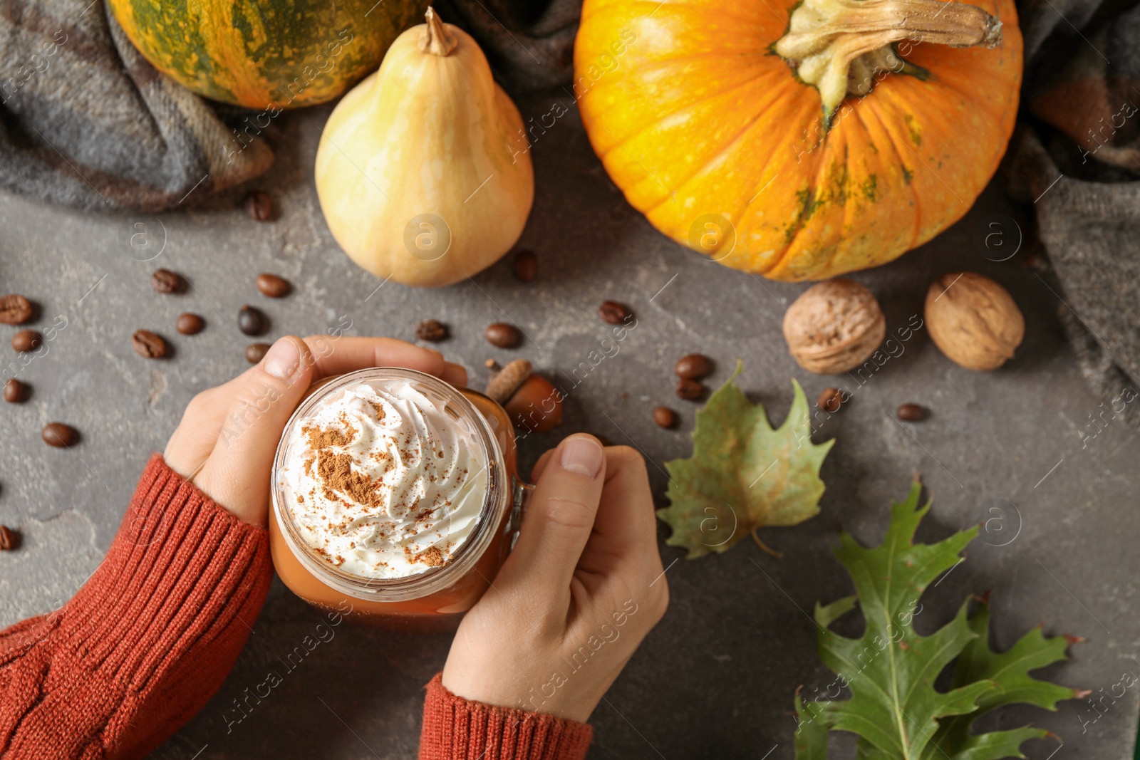 Photo of Woman holding mason jar of tasty pumpkin spice latte at grey table, top view