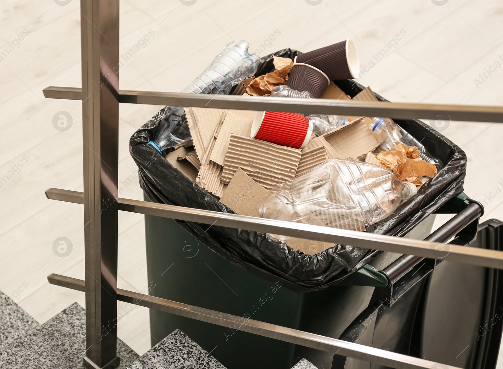 Photo of Full trash bin near stair way indoors. Waste recycling