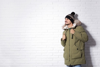 Young man wearing warm clothes against brick wall, space for text. Ready for winter vacation