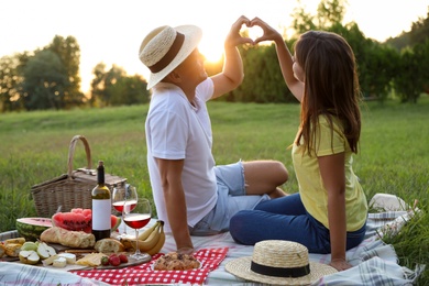 Photo of Happy couple making heart with hands on picnic in park
