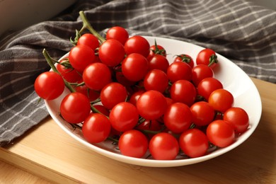 Photo of Plate of ripe whole cherry tomatoes on wooden table, closeup