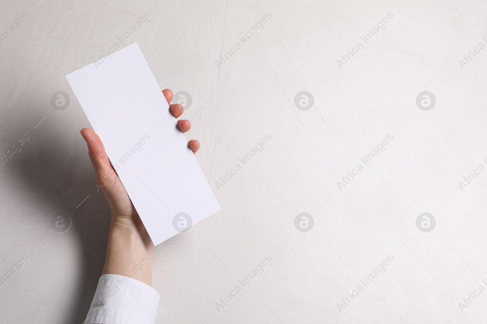 Photo of Woman holding blank card at white table, top view. Mockup for design