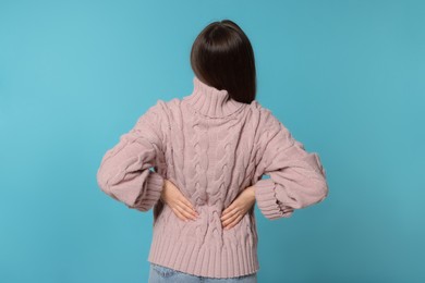 Woman suffering from back pain on light blue background. Arthritis symptoms