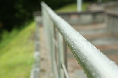 Photo of Rainy weather. Metal handrail with water drops outdoors, closeup. Space for text