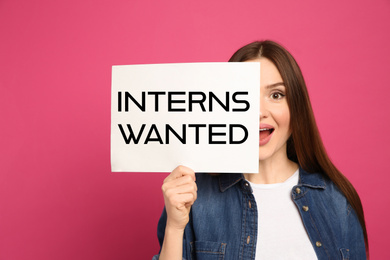 Image of Emotional woman holding paper with text INTERNS WANTED on pink background